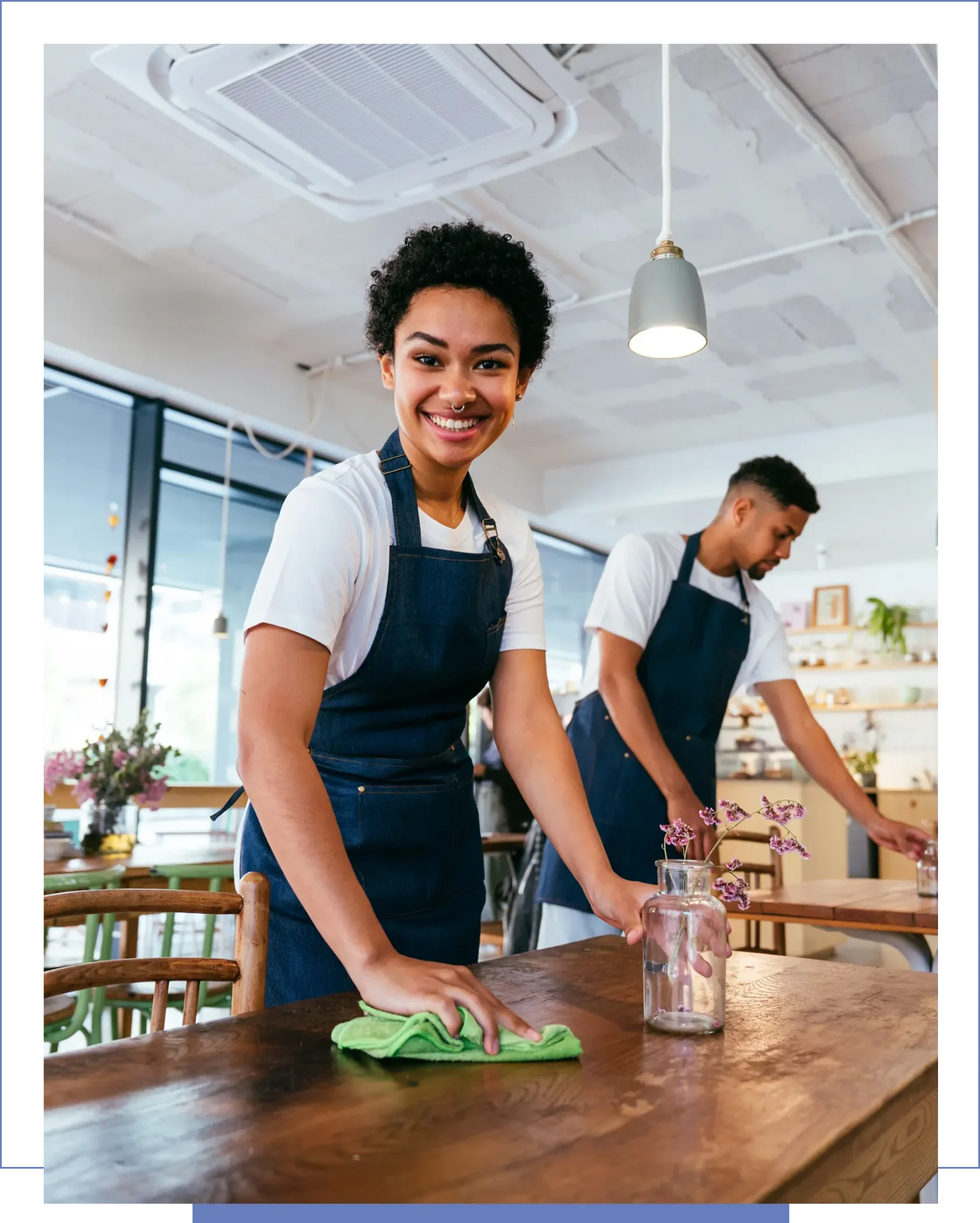 Smiling cafe workers wipe wooden tables.